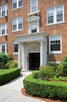 the front entrance of a brick building with bushes and a sidewalk